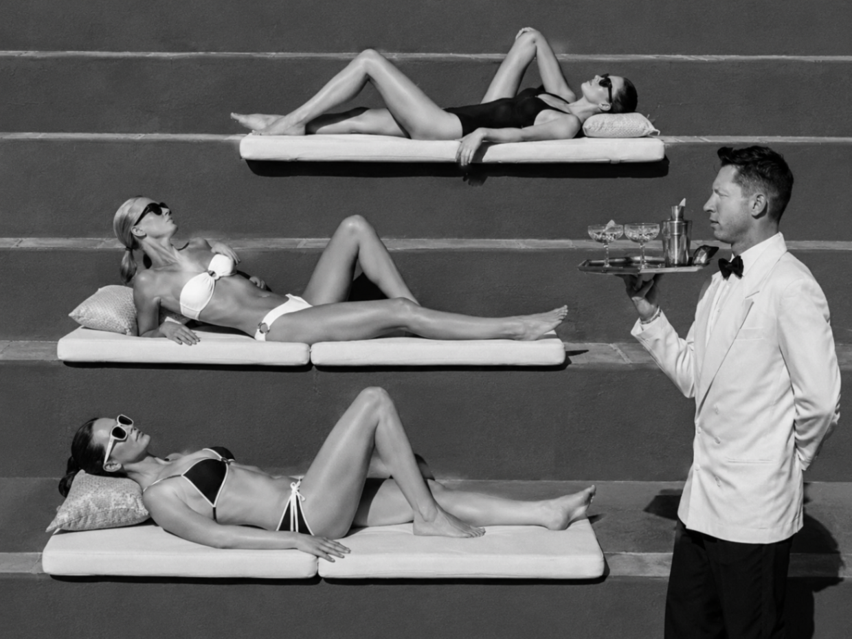 White-jacketed waiter serving cocktails to women reclining on tiered loungers