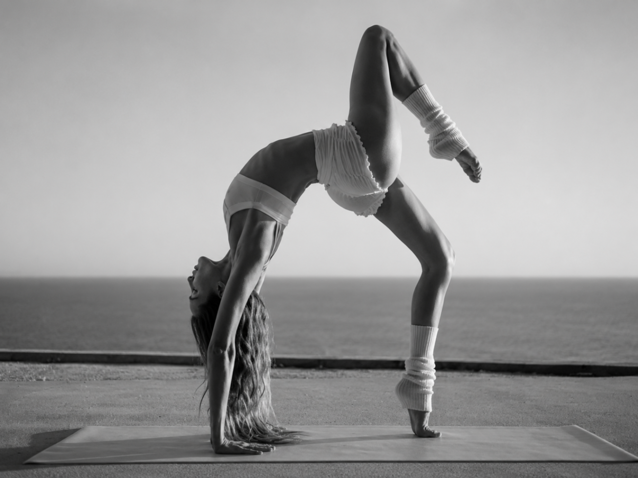 Woman in a graceful backbend on a yoga mat by the ocean