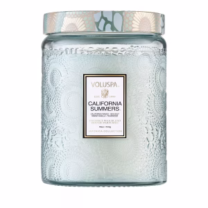 The Voluspa California Summers 18oz Candle comes in a textured clear glass jar with a patterned lid and features a label on the front displaying the candle's name and details in gold and black text.