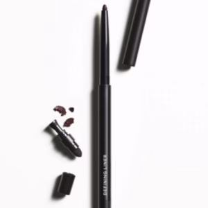 A Revitalash Defining Liner Black pencil with its cap off rests on a white surface, exposing the black tip and nearby smudges; a small smudger is attached to the other end.