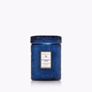 A decorative blue glass jar with an embossed pattern, labeled “Voluspa Mediterranean Lemon 5.5oz Candle,” features a matching blue lid and is set against a plain white background.